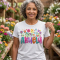 The Beauty Closet cream cotton t-shirt with Abuela floral graphic print worn by a smiling woman in a greenhouse
