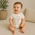 Happy baby wearing a cream The Beauty Closet bodysuit with I Love My Daddy text and a small red heart graphic