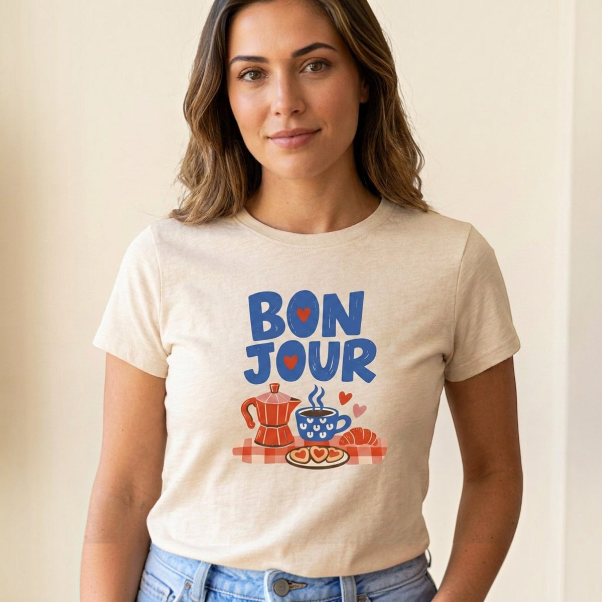 The Beauty Closet beige cotton crewneck t-shirt featuring a Bonjour graphic with coffee, croissant, and heart icons.