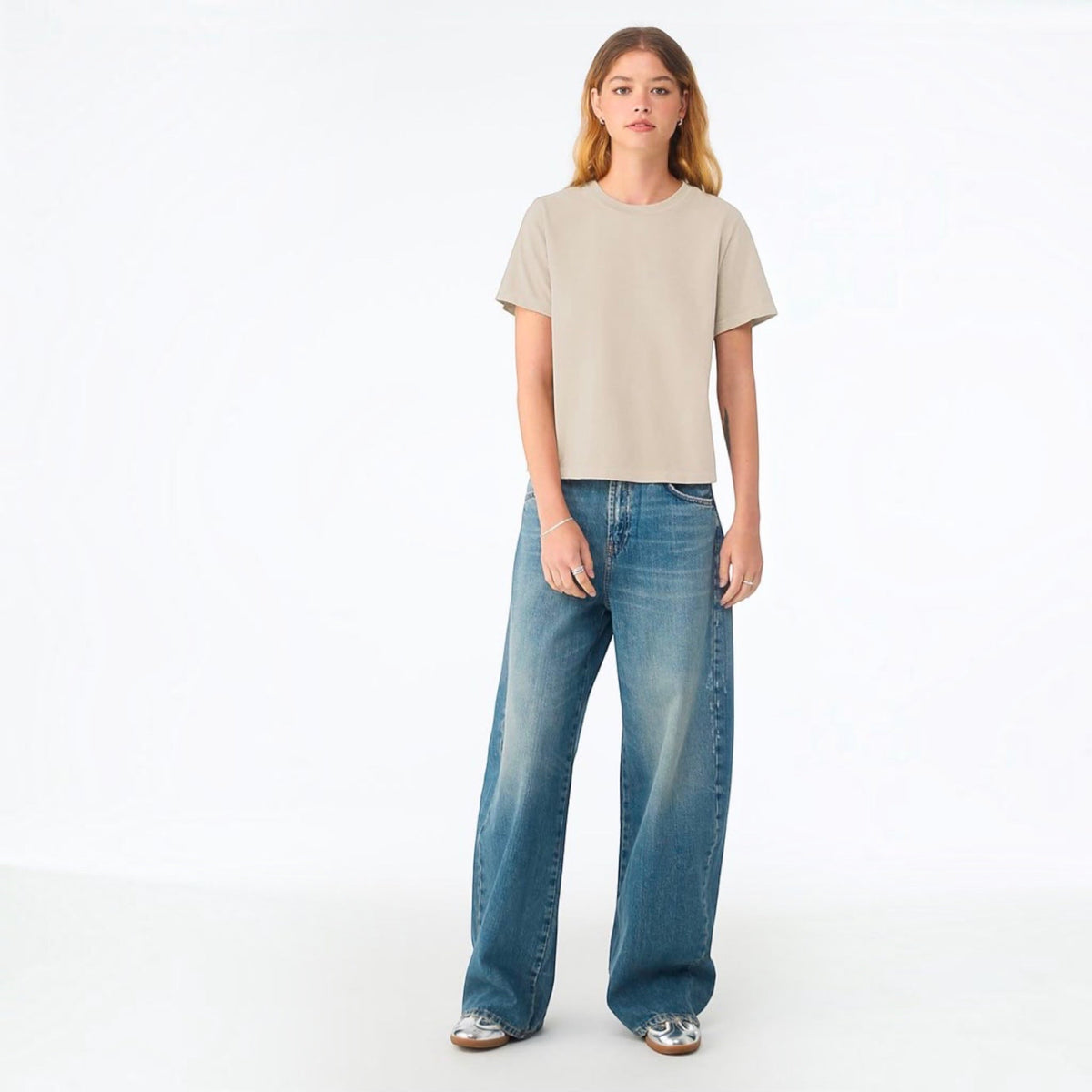 The Beauty Closet model wearing a beige cotton crewneck t-shirt with wide-leg blue jeans against a white background