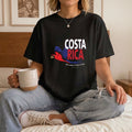 The Beauty Closet black crewneck t-shirt with Costa Rica graphic print, worn by a woman holding a ceramic mug.