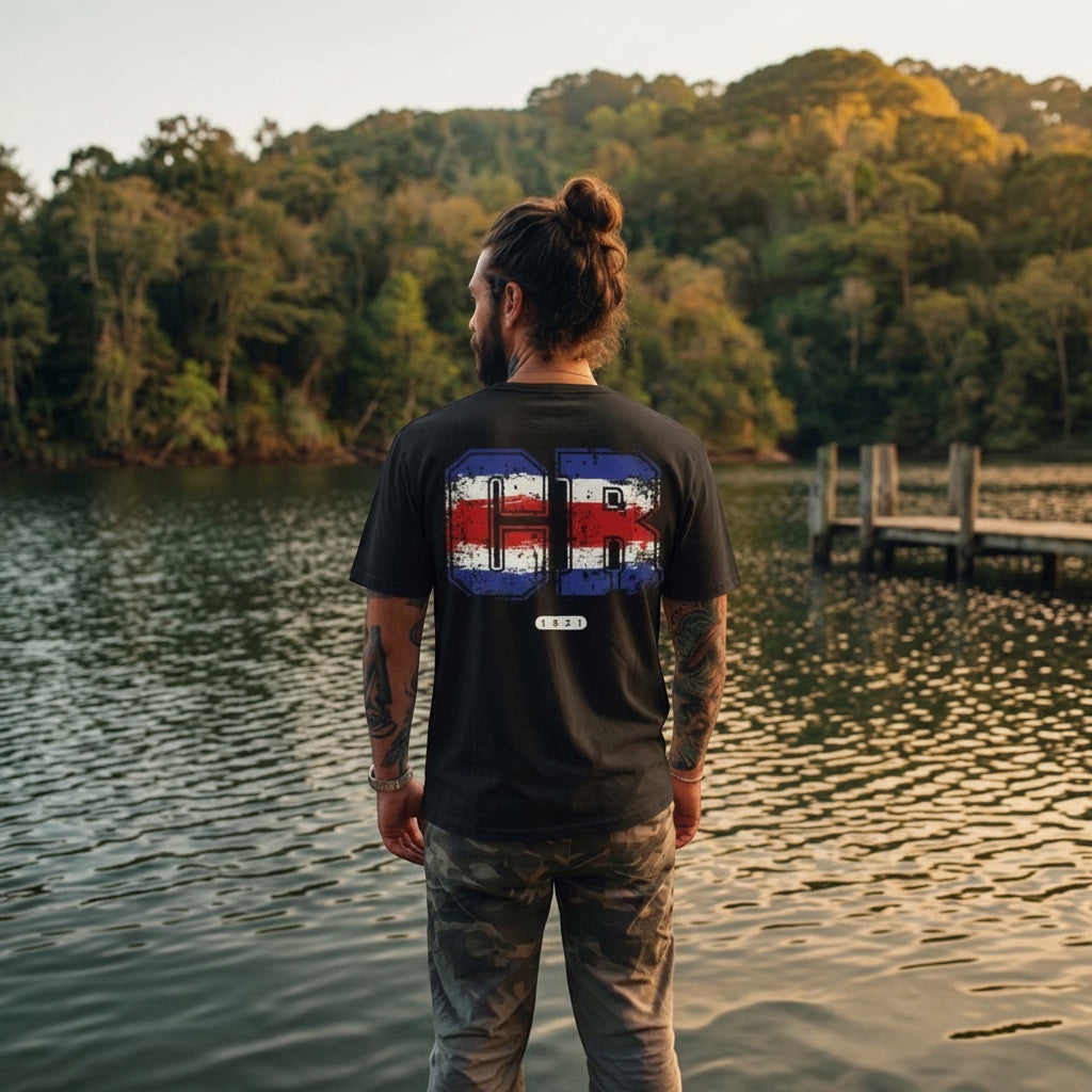 The Beauty Closet black cotton t-shirt with Costa Rica flag graphic on back, worn by a man standing by a lake.