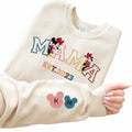 The Beauty Closet cream crewneck sweatshirt featuring a MAMA graphic with Minnie Mouse and EST. 2023 sleeve detail.