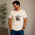 Man wearing a cream-colored The Beauty Closet t-shirt with a Feliz Día Paá fist bump graphic and red hearts.