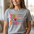 The Beauty Closet grey crewneck t-shirt featuring a colorful She Is Mom graphic print with inspirational text.