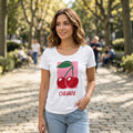 The Beauty Closet white cotton crewneck t-shirt featuring a red cherry graphic print on a pink square background.