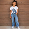 The Beauty Closet white crew neck t-shirt with a blue poodle graphic print worn by a smiling girl with blue jeans.