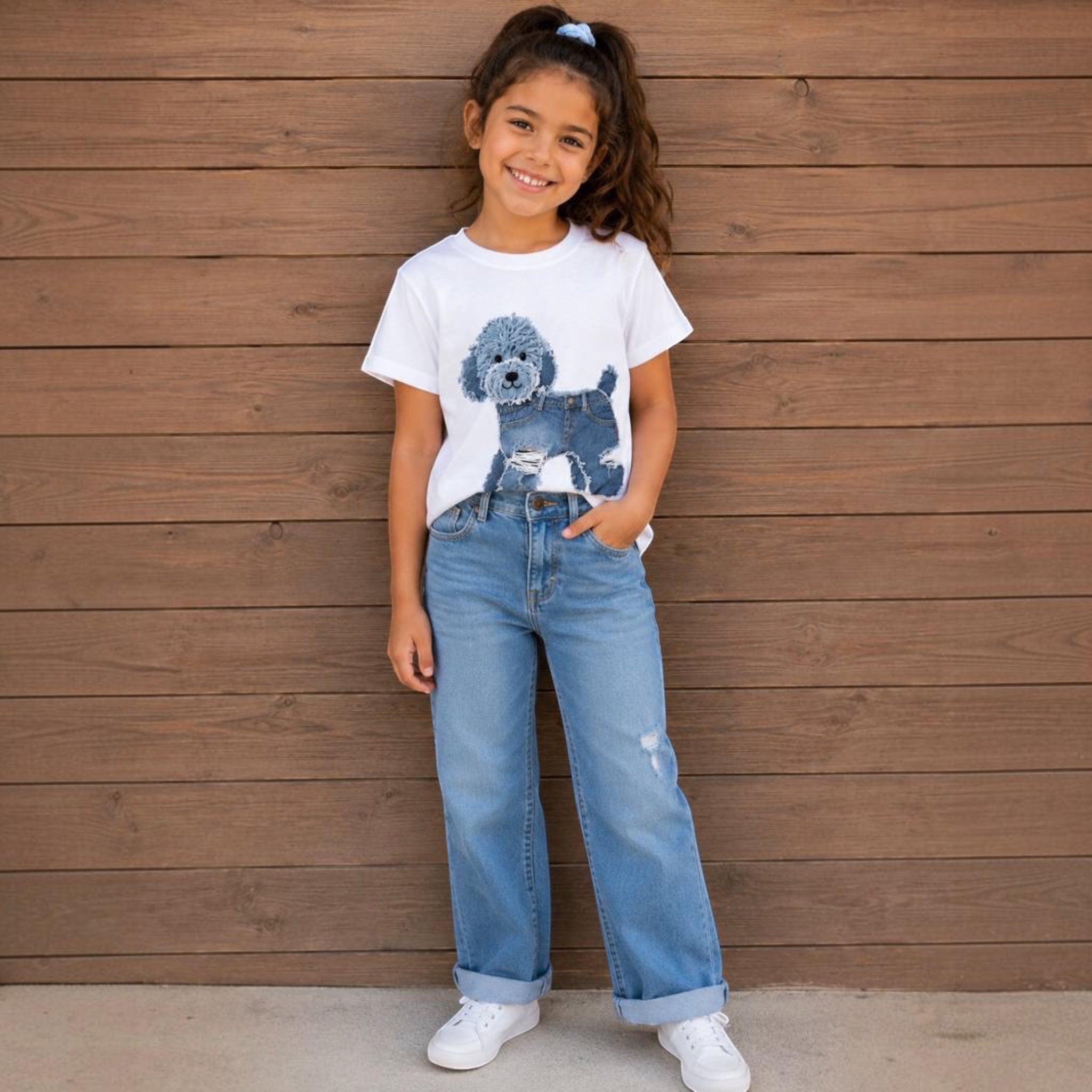 The Beauty Closet white crew neck t-shirt with a blue poodle graphic print worn by a smiling girl with blue jeans.
